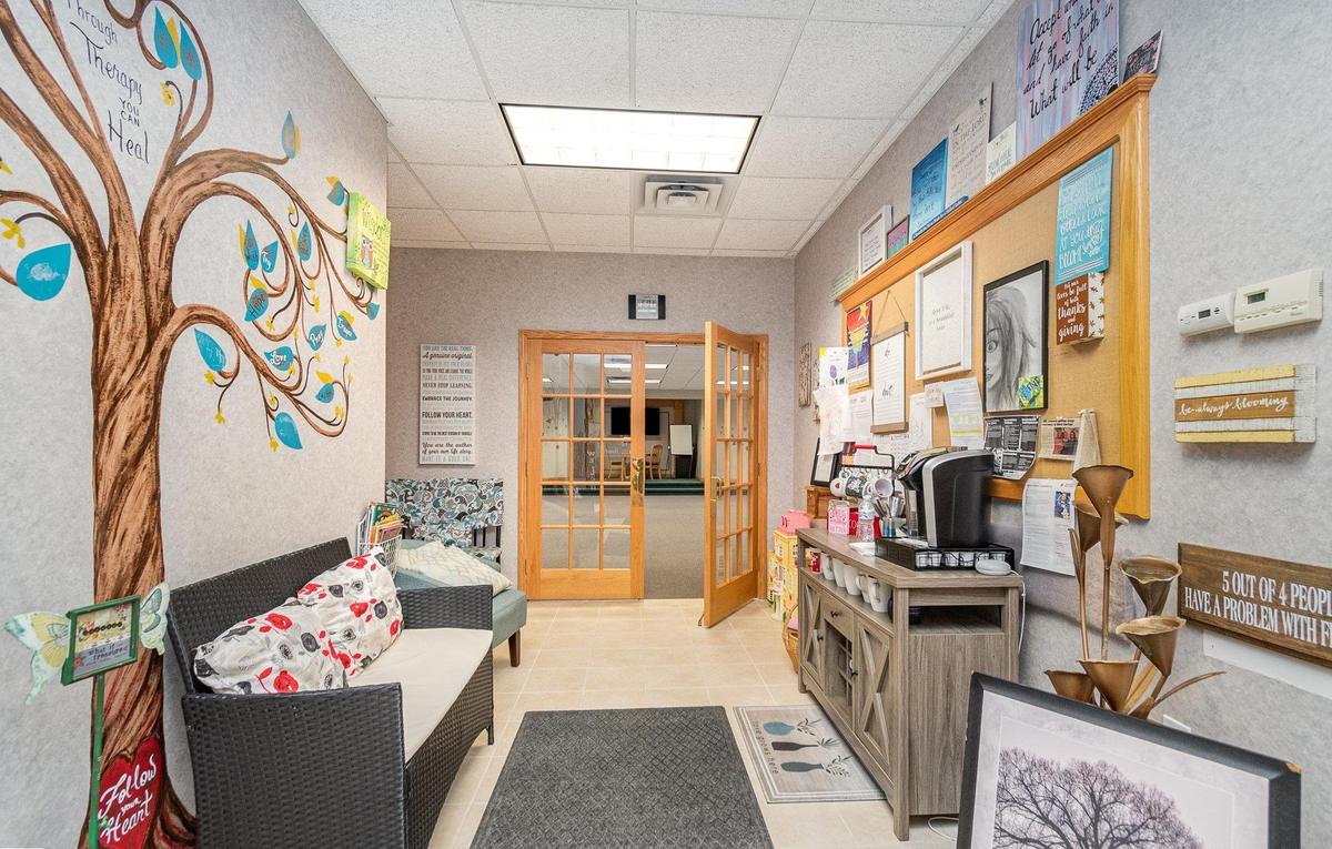 A tree painted along the whole waiting room wall at Blooming Consultants, with the words Through Therapy You Can Heal written through its branches.